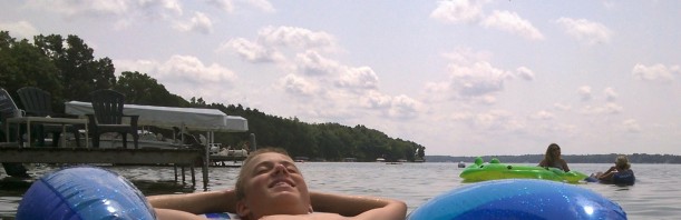 young person floating on summer lake; puffy clouds overhead