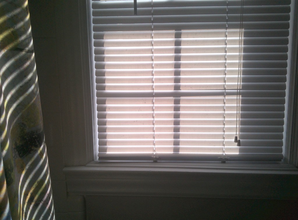 photo of bathroom window with venetian blinds closed and window pane shadows cast upon the slats