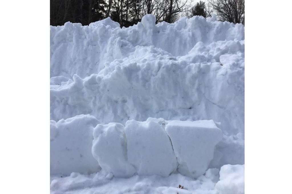 section of snow heaped by parking lot snow plow service forming a lumpy white surface of textures and shadows