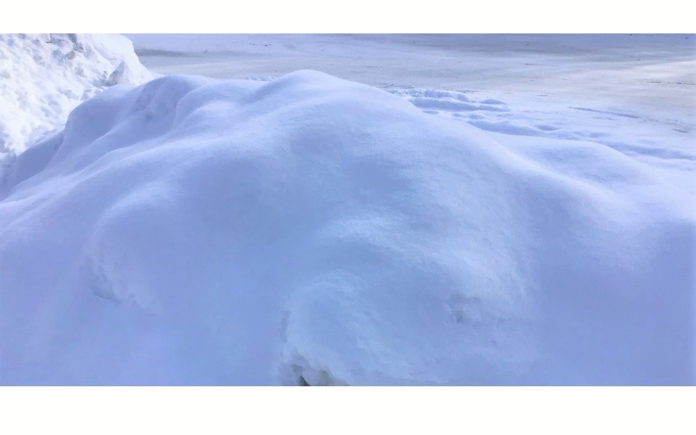 slightly bluish color tone on the lumpy snow pile in the shade at the edge of a plowed parking lot
